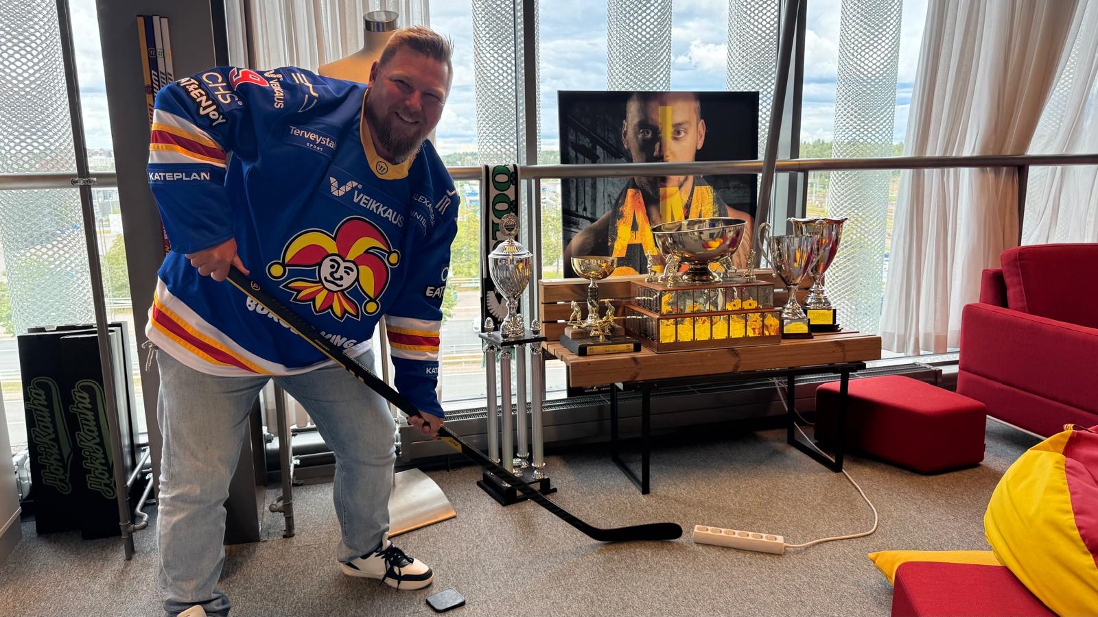 LastBot CEO Janne Timonen holding a hockey stick in a Jokerit jersey at the Jokerit office